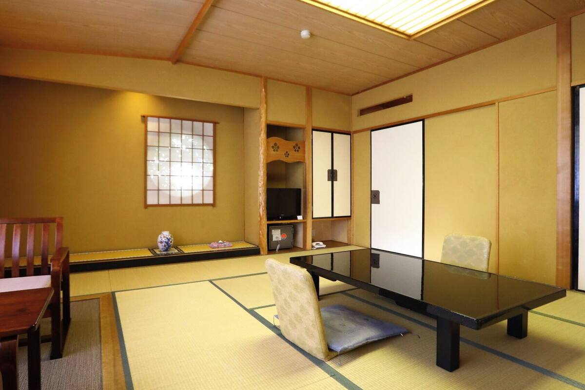 Une pièce de style japonais traditionnel, avec un sol recouvert de tatamis, une table basse, une chaise en bois, un téléviseur et des portes coulissantes.