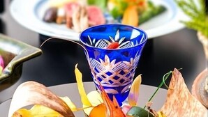 Uma mesa com um centro de mesa de vidro azul decorativo, um prato com comida e um prato branco ao fundo.
