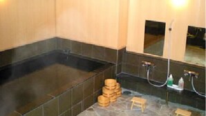A spa room with a large black bathtub, a small wooden stool, and a mirror above the bathtub. - Niigata Park Hotel (Niigata)