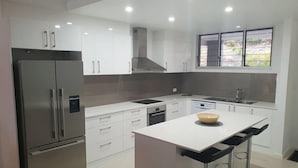 Una cocina moderna con electrodomésticos de acero inoxidable, armarios blancos, una isla central con taburetes y un ventanal con vistas a zonas verdes.