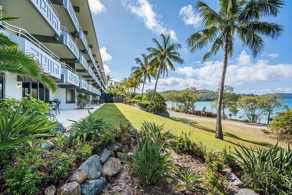 A hotel with multiple balconies, a well-maintained lawn, and a view of the sea. - Frangipani 103 (Whitsundays)