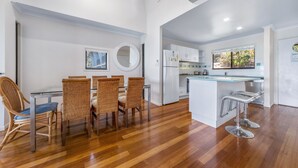 A modern kitchen with a dining area, featuring a round mirror, white cabinets, and a central island with bar stools. - Panorama 12 (Whitsundays)