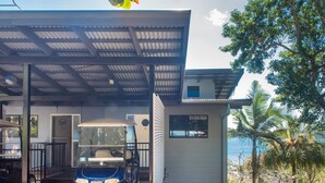 A modern house with a covered porch, a golf cart, and a view of the ocean. - Panorama 12 (Whitsundays)