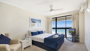 Habitación de hotel con una cama grande, televisión, ventilador de techo y vista al océano.