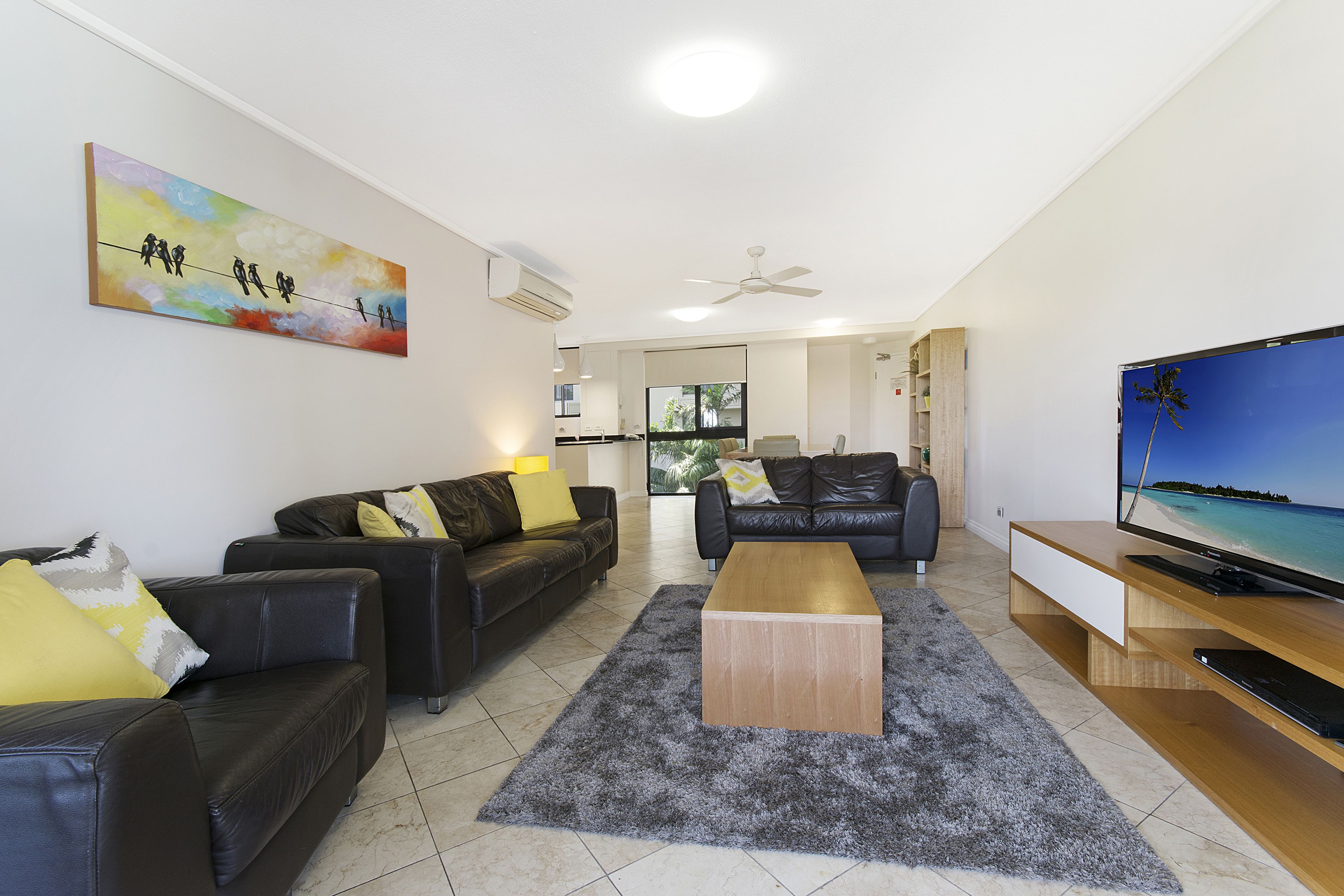 A modern living room with two black leather sofas, a wooden coffee table, a flat-screen TV, and a colorful abstract painting on the wall.