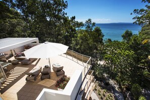 A rooftop terrace with outdoor seating, a view of the sea, and surrounding greenery.