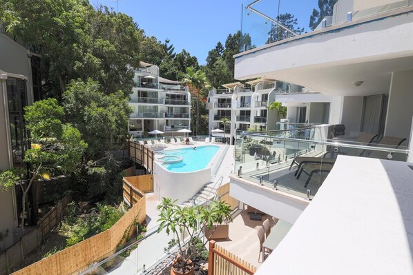 A modern apartment complex with a central swimming pool, multiple balconies, and lush greenery surrounding the buildings.