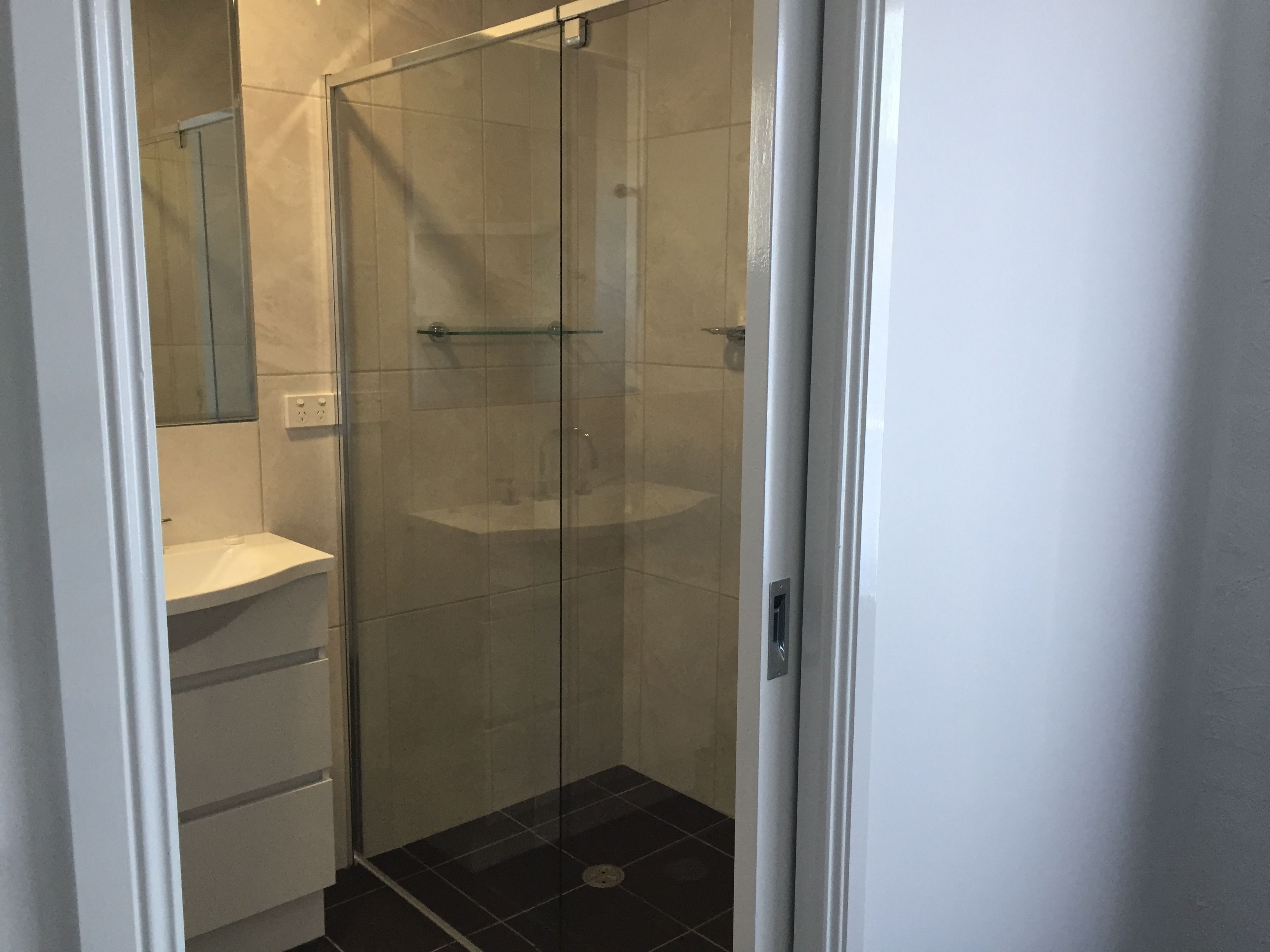 Une cabine de douche fermée par des parois en verre, avec un lavabo blanc et un miroir au mur.