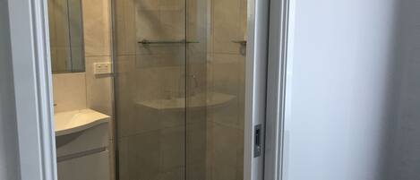Une cabine de douche fermée par des parois en verre, avec un lavabo blanc et un miroir au mur.