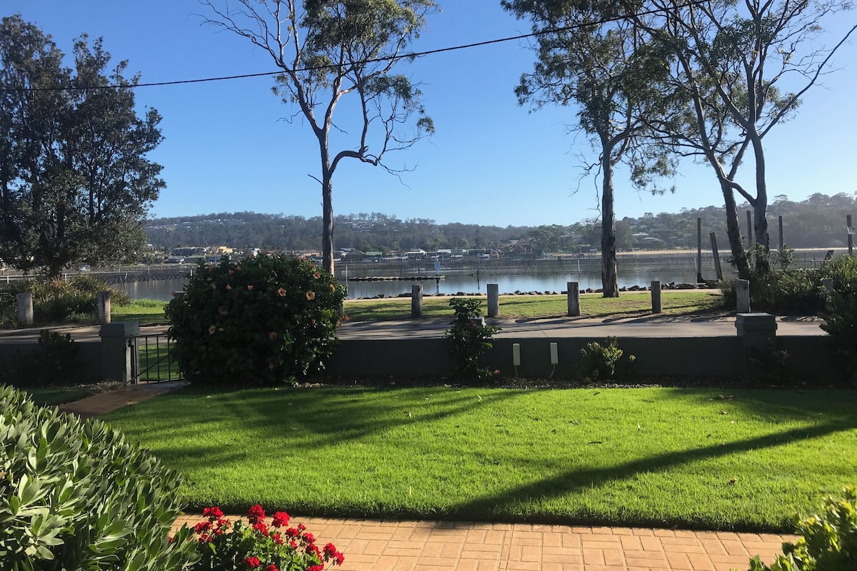 A landscaped outdoor area with a grassy lawn, trees, and a view of a body of water.