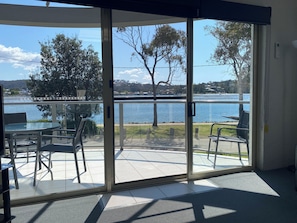 Ein Zimmer mit einer Glasschiebetür, die auf eine Außenpatio mit Tisch und Stühlen führt, mit Blick auf einen See und einer Brücke in der Ferne.