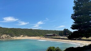 Paisatge costaner amb una platja, aigua blau clar i un edifici a la distància.
