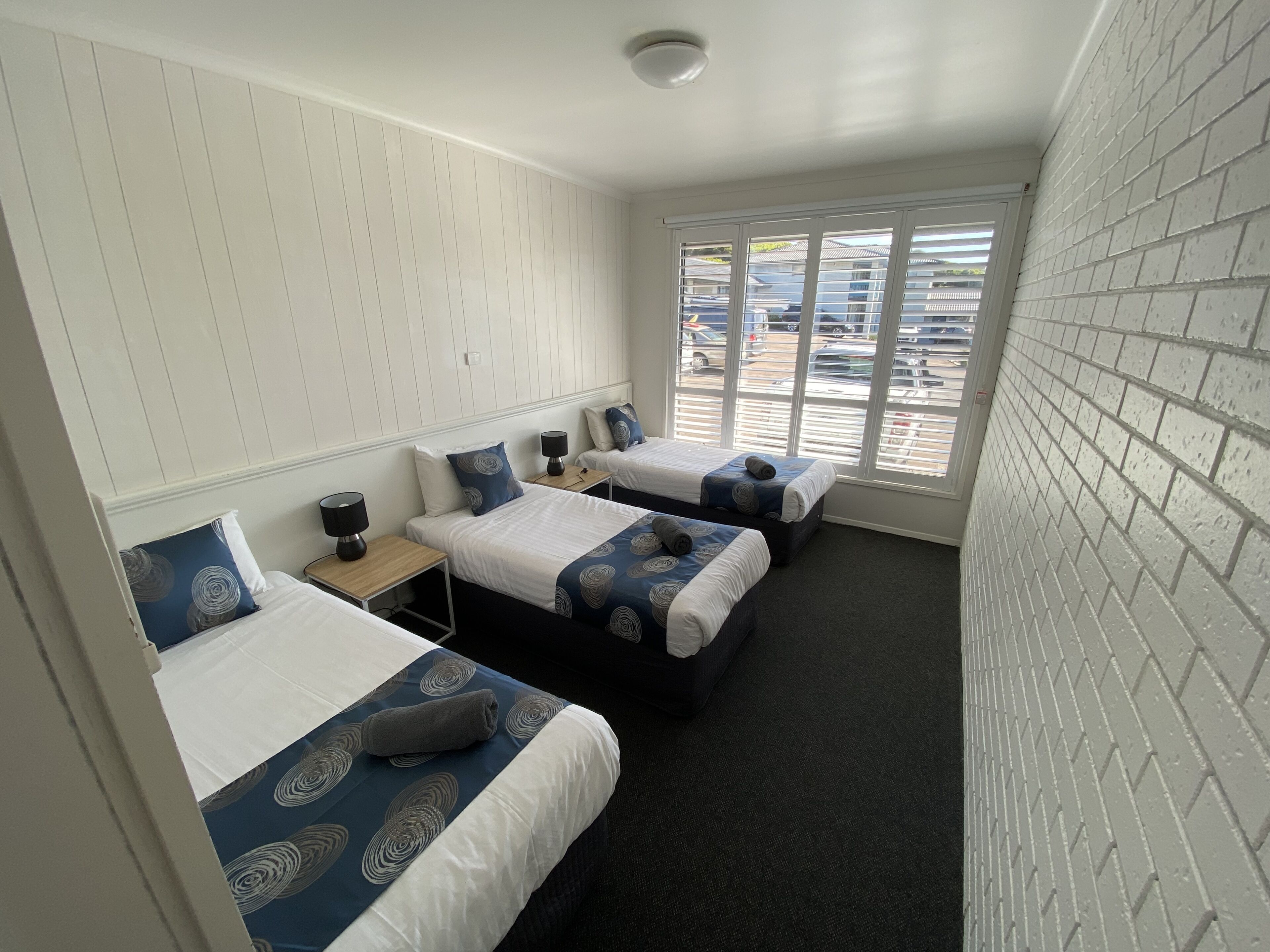 A hotel room with two beds, a small table, and a window with blinds.