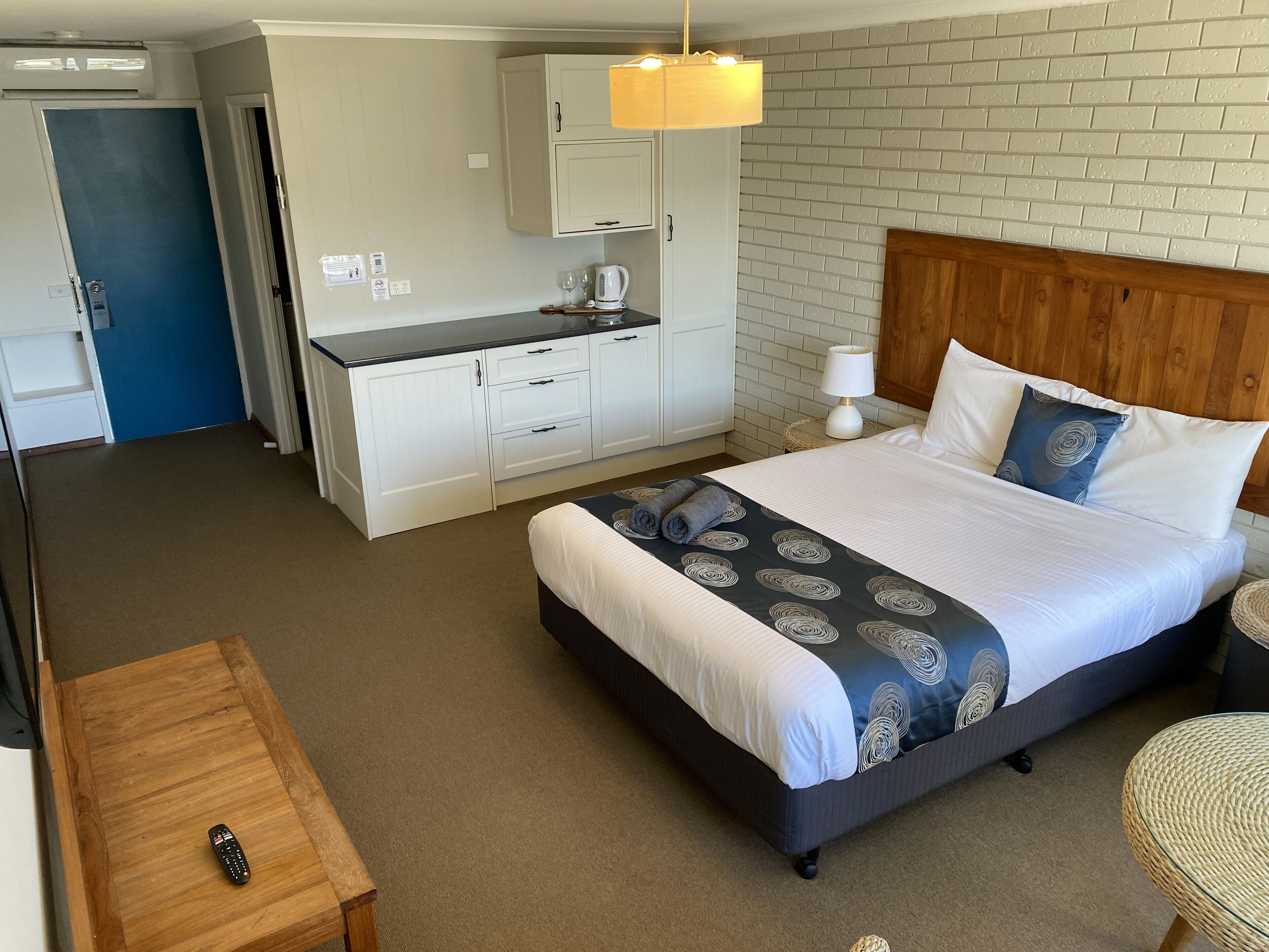 A hotel room with a bed, a desk, a chair, a kitchenette, and a bathroom.
