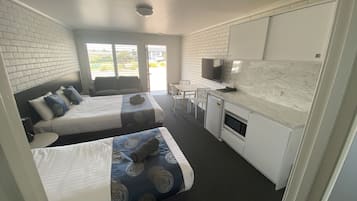 A hotel room with two beds, a kitchenette, a TV, and a view of the outside.