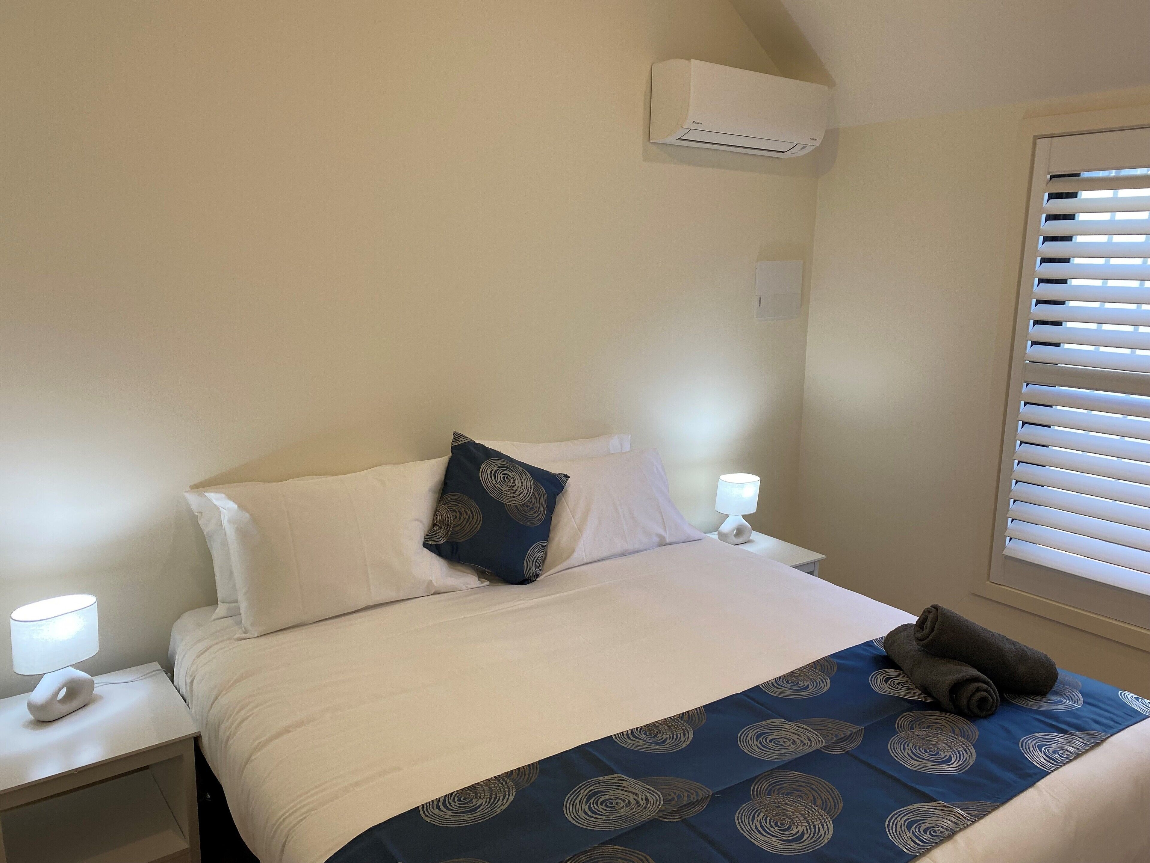 Hotelkamer met een bed, nachtkastje met lamp, raam met zonwering en een airconditioning aan de muur.