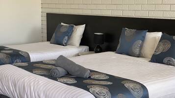 A hotel room with two beds, each with a headboard, and a nightstand with a lamp.