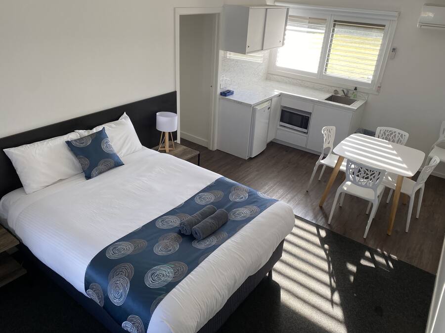 Una habitación de hotel compacta con una cama, una kitchenette pequeña, un área de comedor y una ventana.