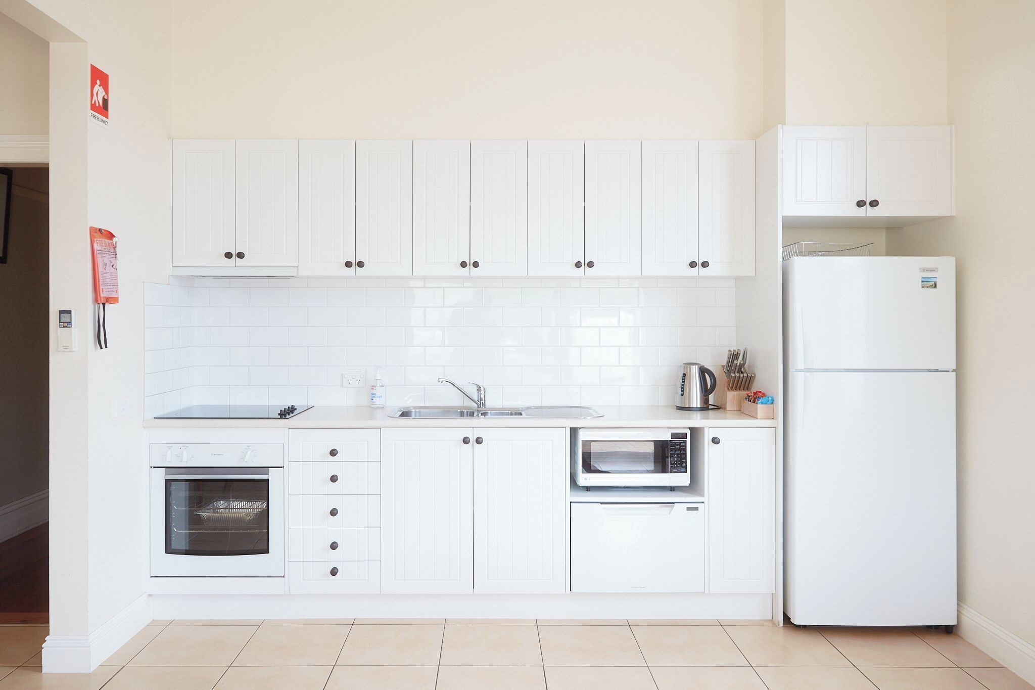 A modern kitchen with white cabinets, a built-in oven, a microwave, and a refrigerator.