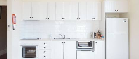 A modern kitchen with white cabinets, a built-in oven, a microwave, and a refrigerator.