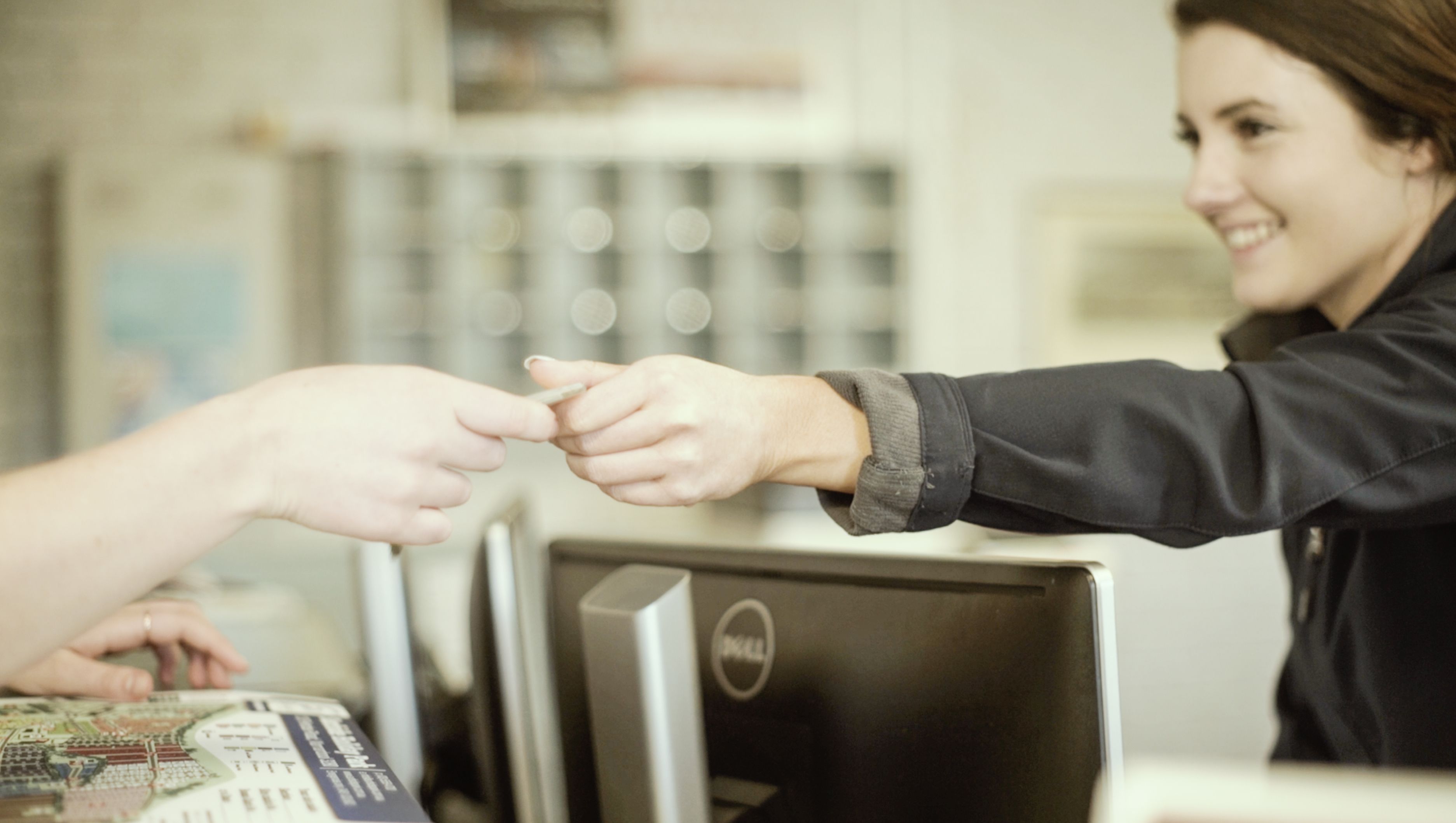 A person handing over a card to another person at a counter with a computer and a menu in the background.