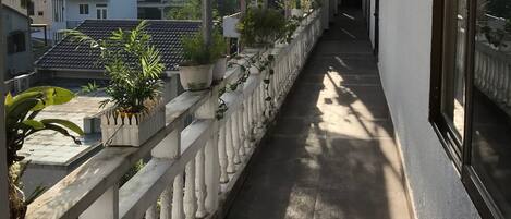 Un balcón con plantas en macetas, barandilla y vista de edificios al fondo.
