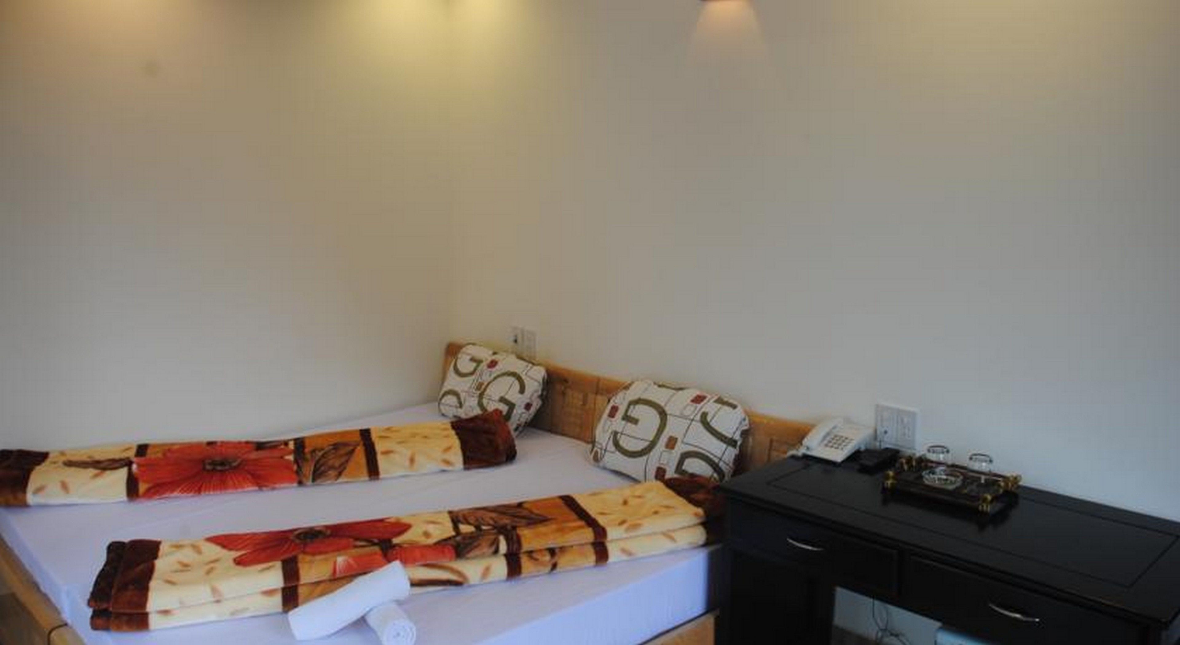 Uma cama de solteiro com roupa de cama estampada, uma mesa de cabeceira com telefone e uma pequena escrivaninha com abajur.