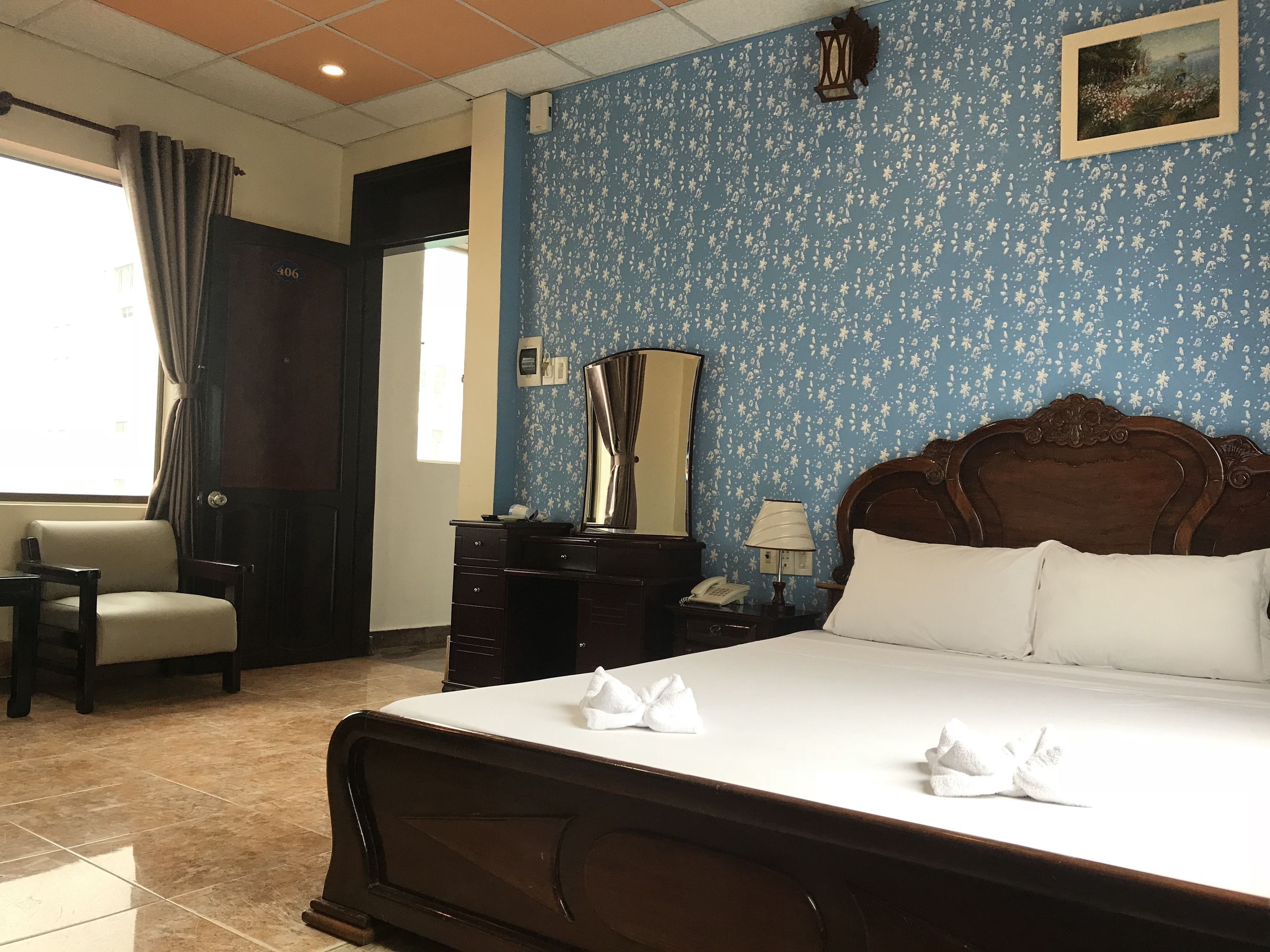 Habitación de hotel con cama, una silla, cómoda, espejo y ventana con cortinas.