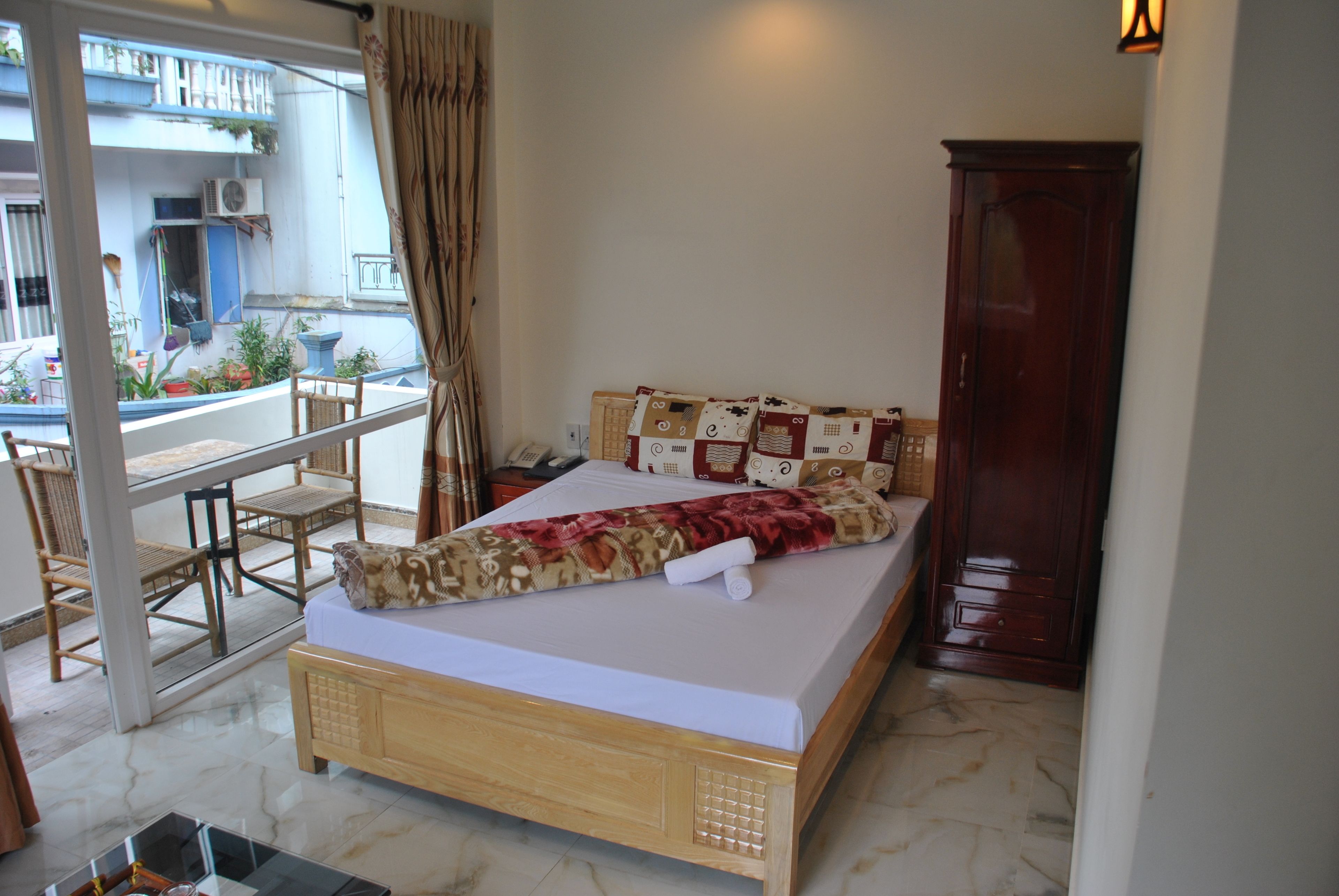Quarto com cama de madeira, varanda com mesa e cadeiras, e vista para o exterior.