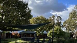 A swimming pool with a brick border, surrounded by grass and a fence. - Greenways Holiday Units (Tocumwal)