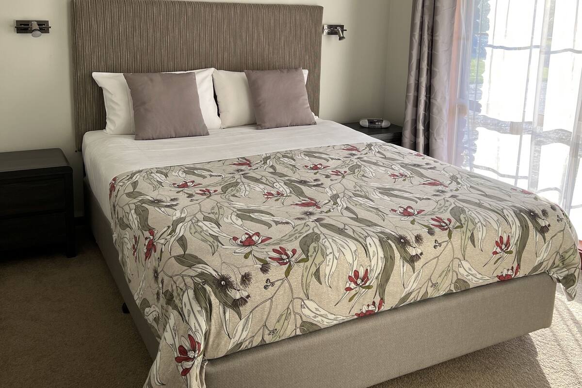 A bedroom with a large bed, a ceiling fan, a painting of birds, and a window with curtains.