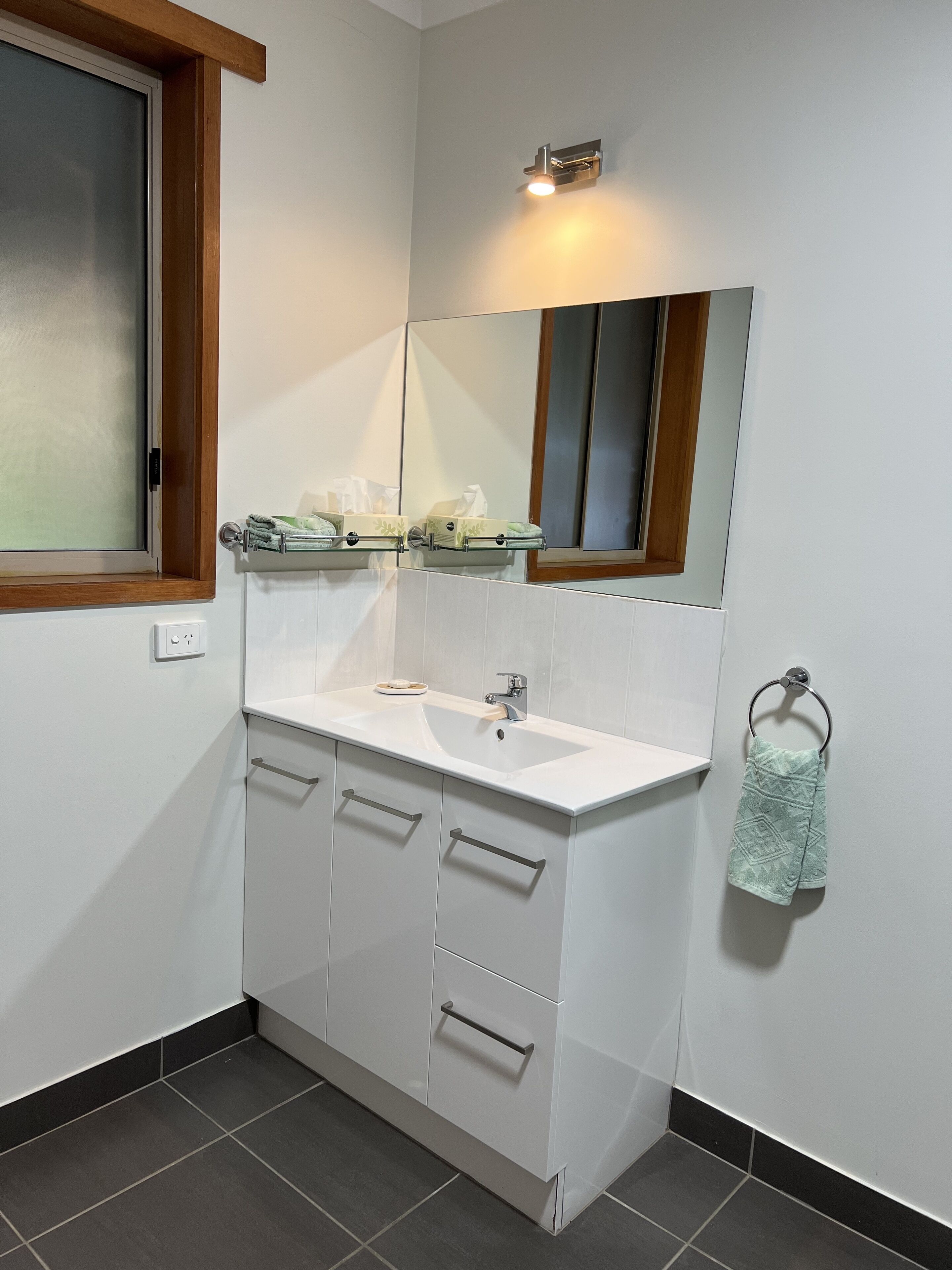 Un baño moderno con un lavamanos blanco, dos cajones, un espejo y un perchero para toallas.