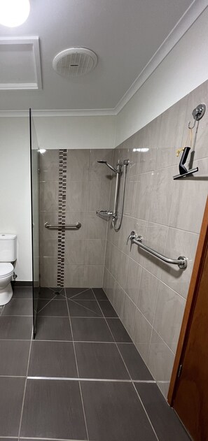A modern bathroom with a glass shower enclosure, grab bars, a toilet, and a towel rack. - Greenways Holiday Units (Tocumwal)