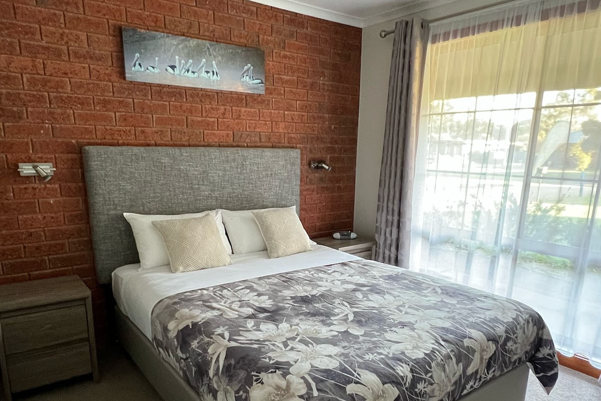 A bedroom with a brick wall, a bed with a floral bedspread, a nightstand, and a ceiling fan.