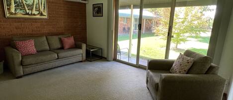A living room with a brick wall, two sofas, a painting, and a sliding glass door leading to a patio.