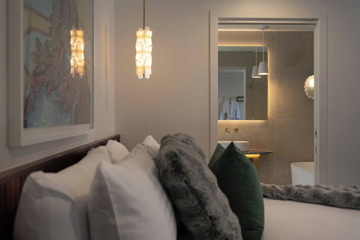 A hotel room with a bed, pillows, a framed picture, and a bathroom visible through an open door.