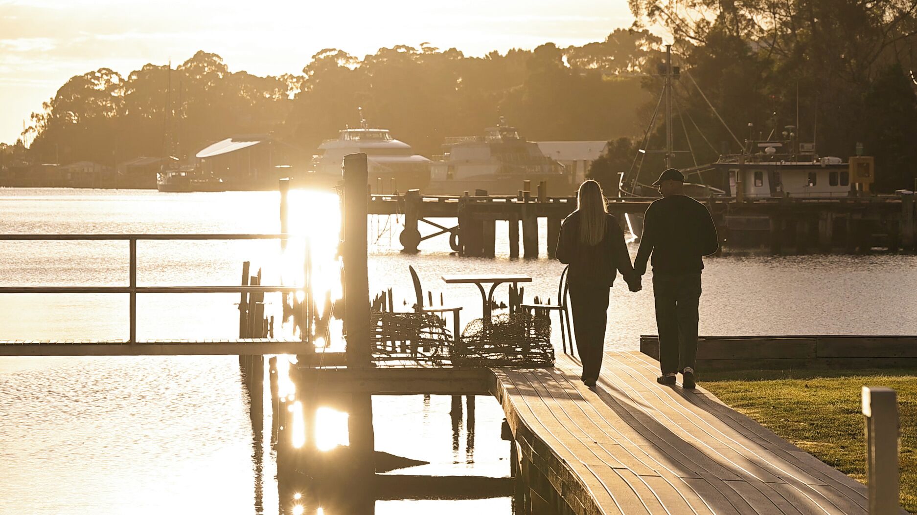 A couple walking on a wooden dock at sunset.