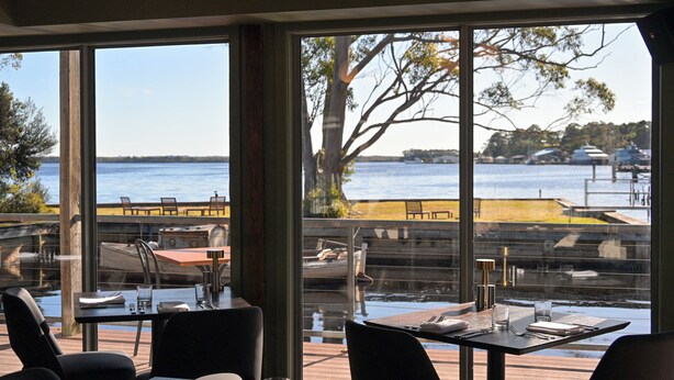 Un restaurante con terraza al aire libre, con vistas a un cuerpo de agua, con mesas y sillas y vista al paseo marítimo.