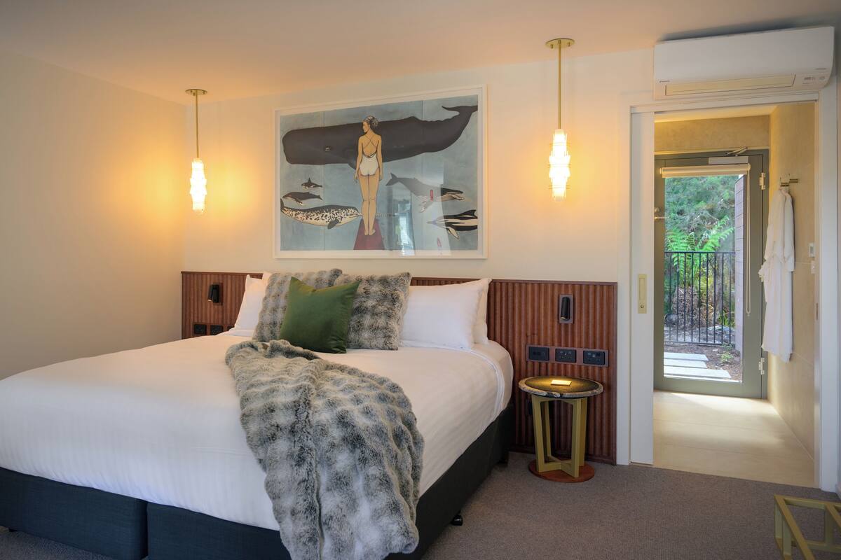 A hotel room with a large bed, a painting of marine life, a small round table, and a door leading to a balcony.