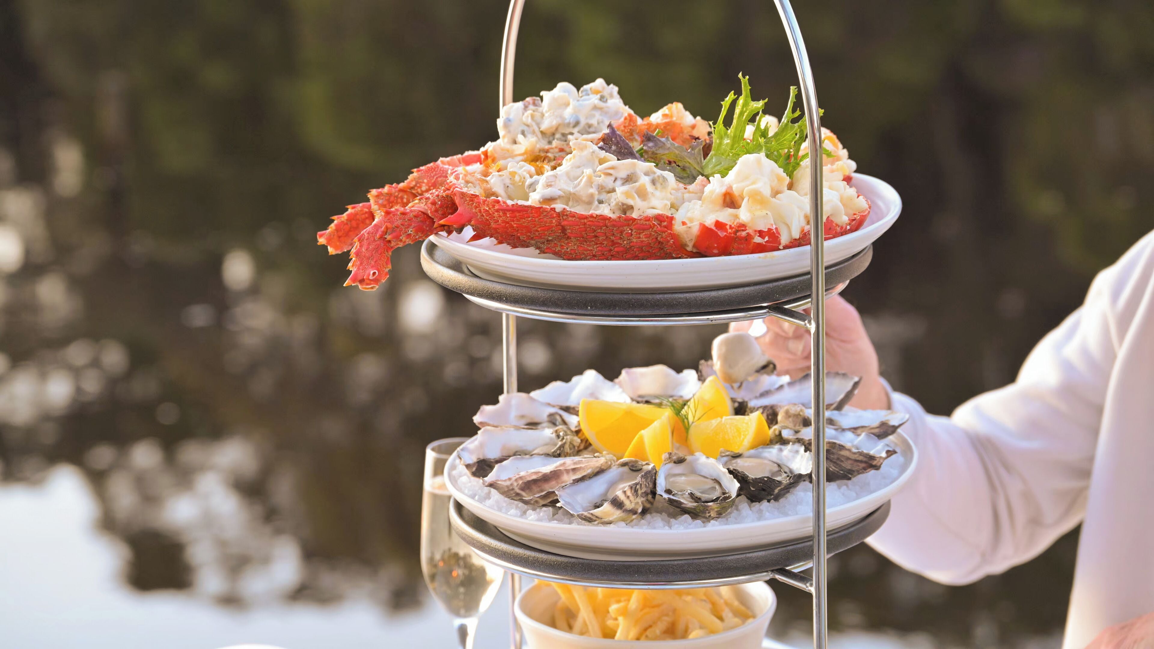 A three-tiered seafood platter with oysters, shrimp, and a salad, held by a person.