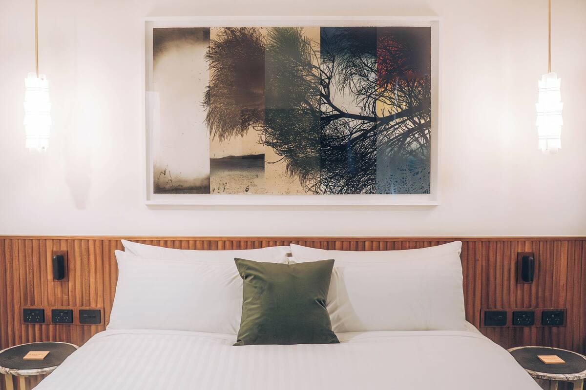 A hotel room with a bed, a wall-mounted artwork, bedside tables, and a wooden headboard.