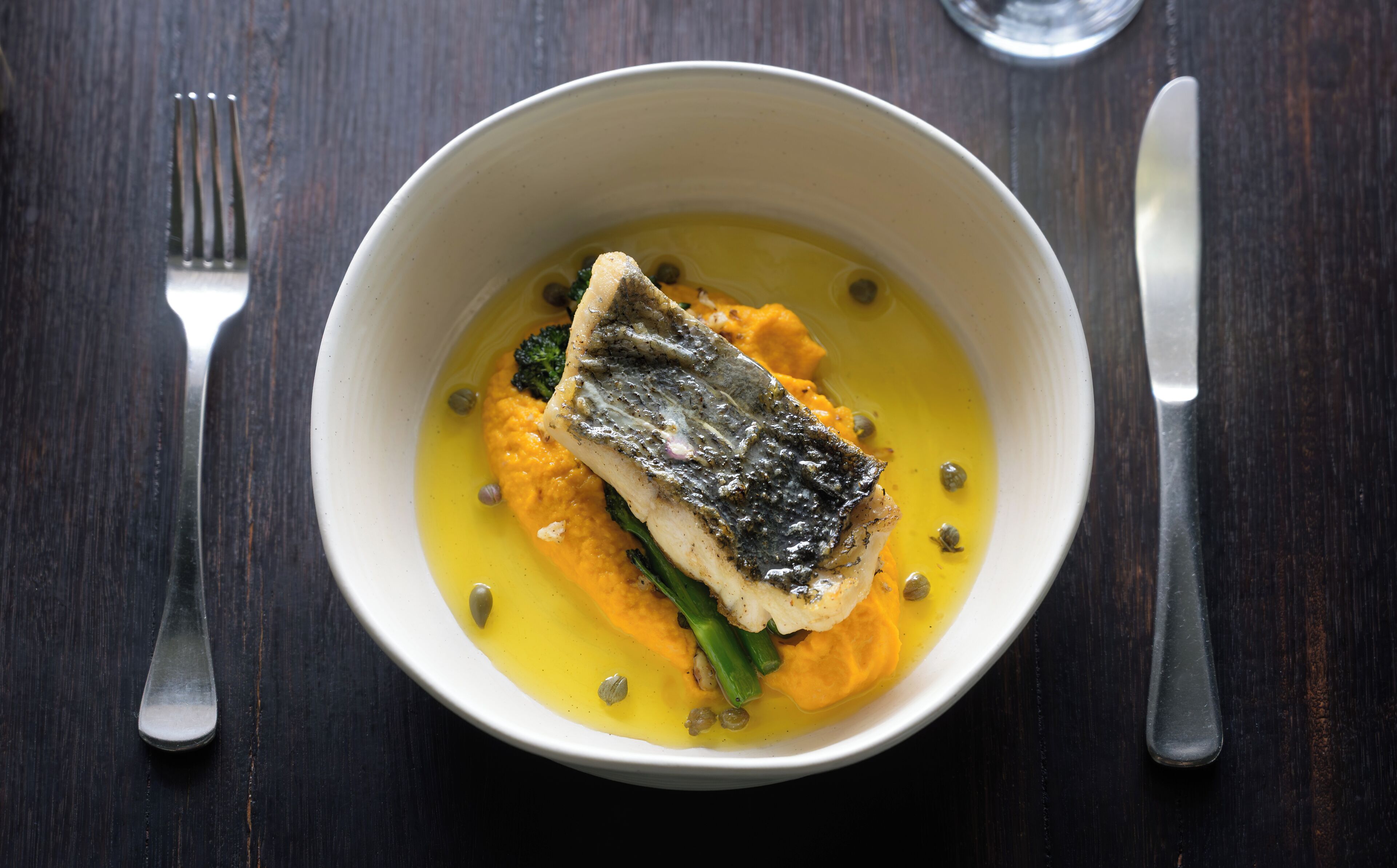 A bowl of food with fish, vegetables, and a yellow sauce.