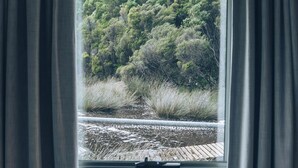 Una ventana con cortinas, vista a un área boscosa y una terraza de madera.