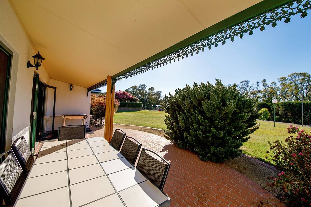 A covered patio with a table and chairs, a view of a well-maintained lawn, and a large bush.
