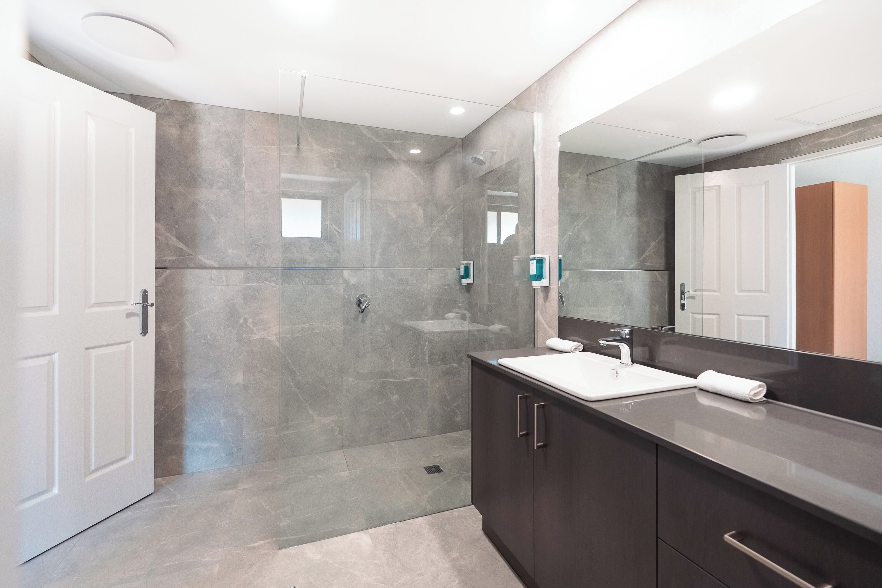 A modern bathroom with a large mirror, a shower, and a vanity with a sink.