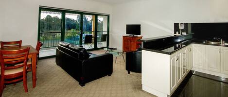 A spacious living area with a dining table, a black leather sofa, and a kitchen with white cabinets and a black countertop.