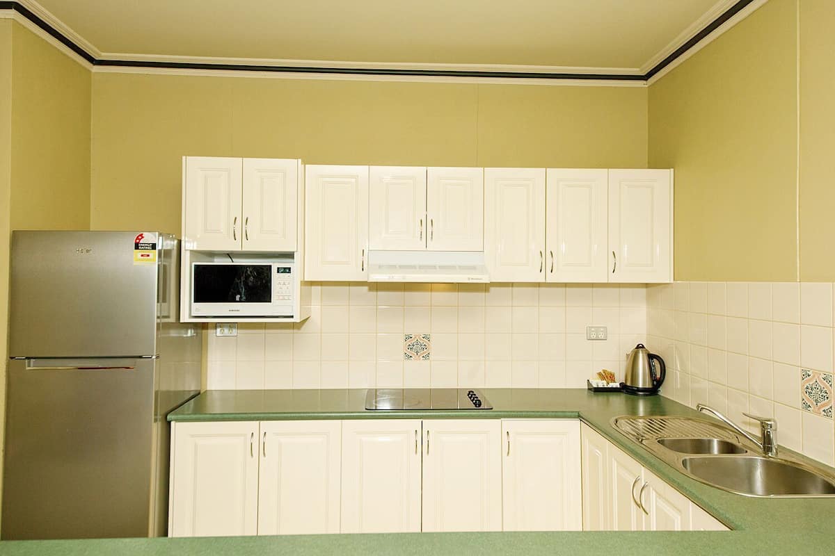 A kitchen with white cabinets, a stainless steel refrigerator, a microwave, and a sink.