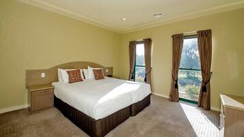 A bedroom with a large bed, a nightstand, a dresser, and a window with curtains.