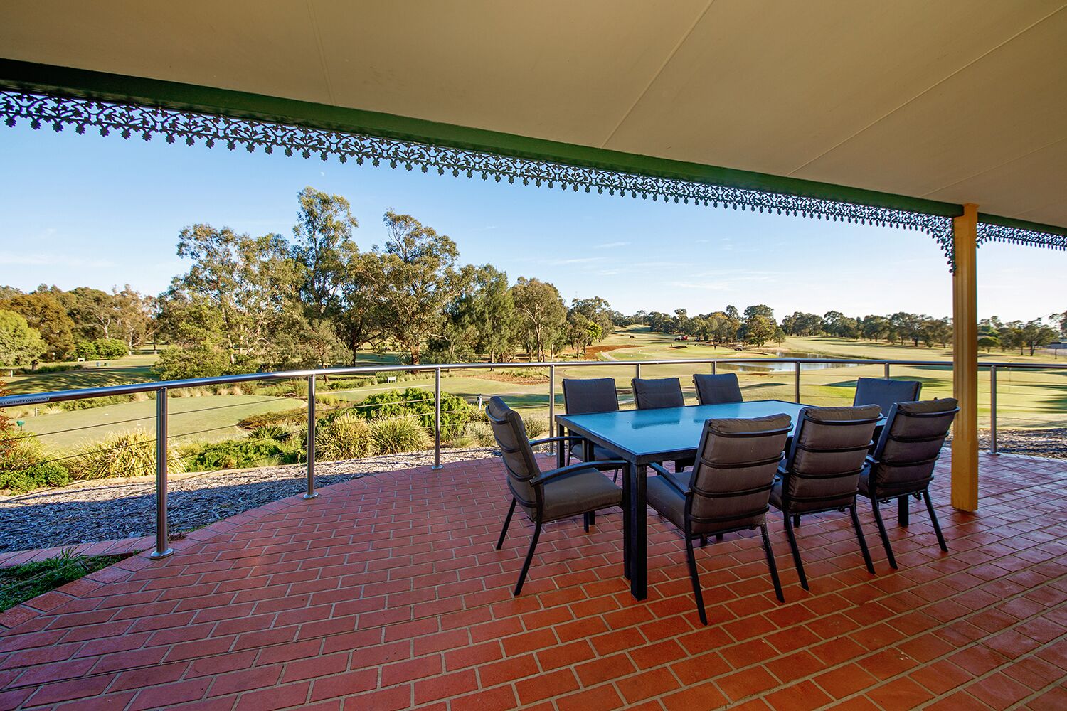 A covered patio with a table and chairs overlooking a golf course.