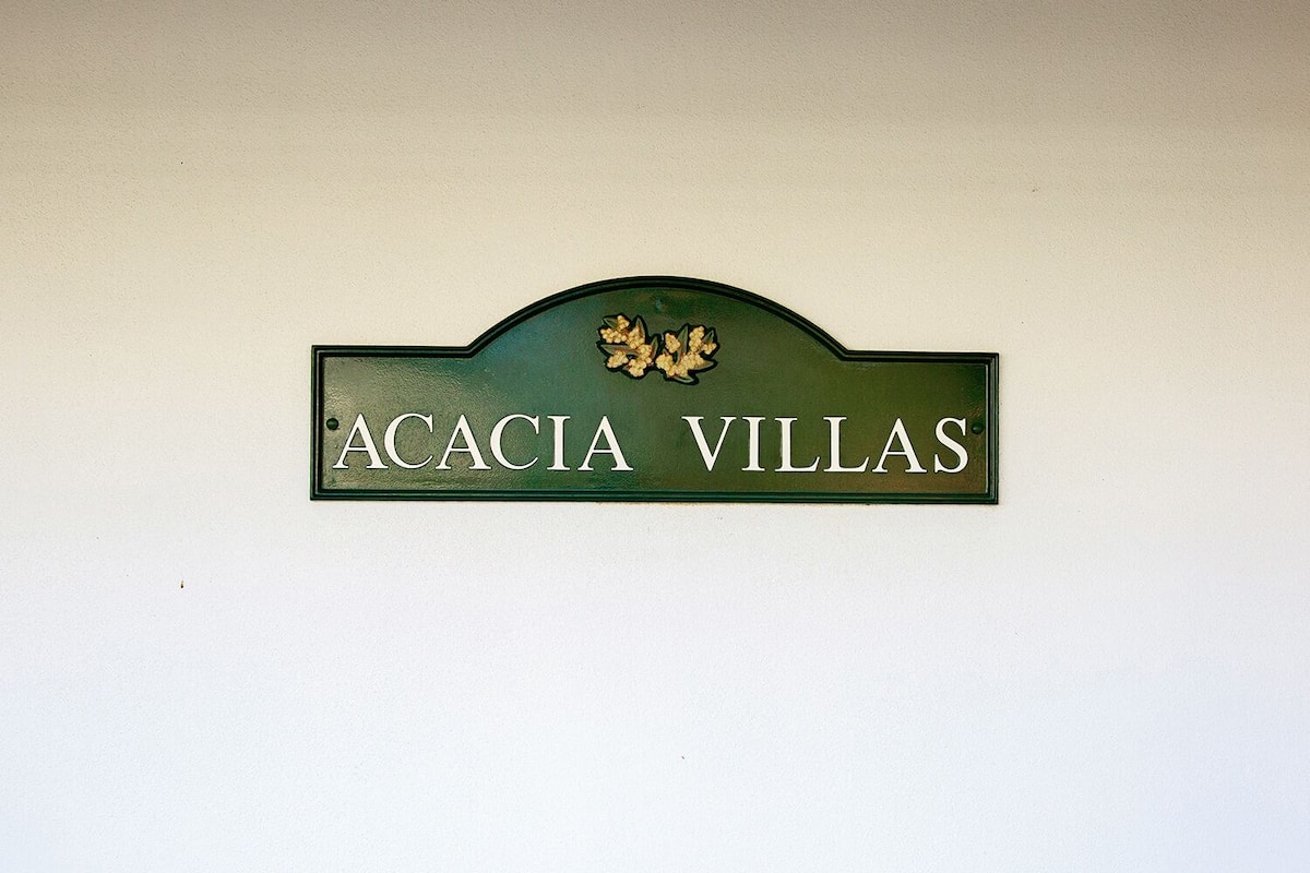 A sign with the text "ACACIA VILLAS" on a white wall.